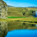 Icelandic nature scenery featuring waterfalls, green hills, and reflective water in a serene landscape. Tranquil Icelandic landscape with waterfalls and lush green hills in the distance.