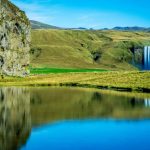 Icelandic nature scenery featuring waterfalls, green hills, and reflective water in a serene landscape. Tranquil Icelandic landscape with waterfalls and lush green hills in the distance.