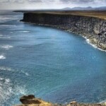 Scenic coastal cliffs with ocean waves hitting the shoreline. Rich coastal cliffside overlooking a deep blue ocean cove.