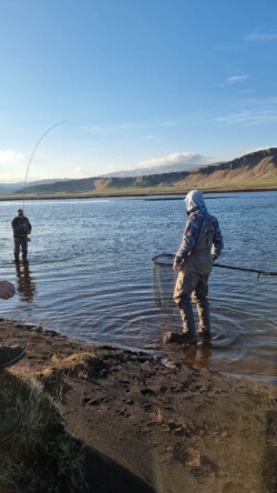 Enjoy fishing with friends at a beautiful river landscape, capturing outdoor angling adventures. Fishermen casting nets in a scenic river setting with mountains and blue sky in the background.