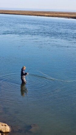 A fisherman casts his line into a peaceful body of water in an outdoor fishing scene. Fishing in a large freshwater lake or river with a person casting a line.