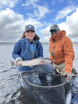 Happy anglers with a freshly caught rainbow trout in a beautiful lake setting, highlighting fishing success and aquatic harvest. Freshly caught rainbow trout with anglers in the background, showcasing quality fish for fishing enthusiasts and aquaculture.