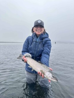 Smiling woman proudly displaying a fish she caught while fishing in cold weather. Young woman holding a large caught fish while fishing in cold water, smiling after successful catch.