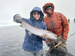 A smiling woman and man in rain gear display a big fish caught during a fishing trip, emphasizing angling, fishing gear, and outdoor activity. Vibrant photo of two anglers holding a large fish on a cloudy day, engaging in freshwater fishing adventure.