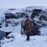Snow-covered canyon with a hunter in winter gear by icy waters. Snowy canyon with a person holding a rifle during winter.