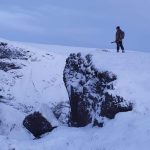 Snowy mountain landscape with a hiker standing on the edge overlooking icy cliffs. Bright winter mountain landscape with a hiker overlooking snowy terrain and rocky cliffs.